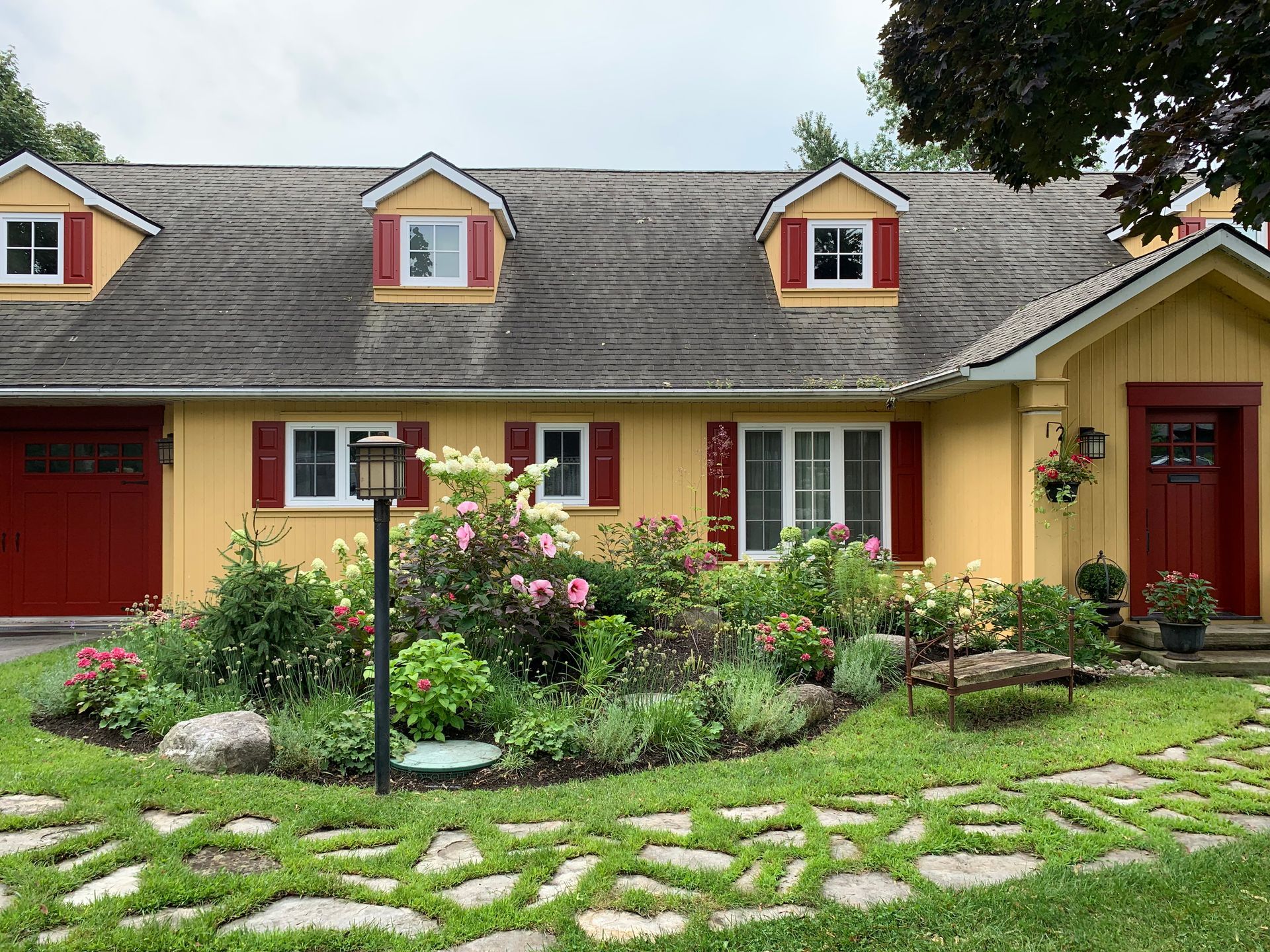 Une maison jaune avec des volets rouges et une porte de garage rouge