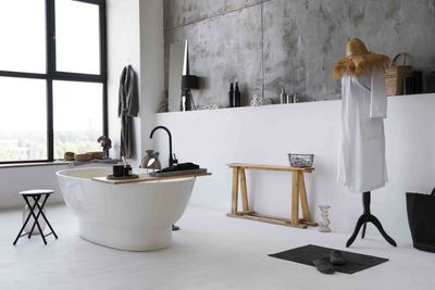 A modern bathroom with light blue walls and a large round mirror over a concrete vanity. A shower and bathtub are visible through a glass door.