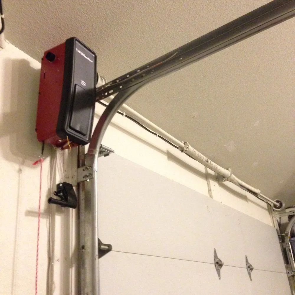Red garage door opener mounted on the ceiling beside a white garage door