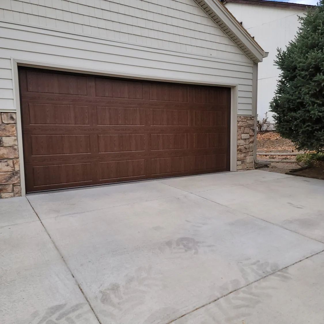 Driveway leading to a brown garage door on a beige house with stone accents.