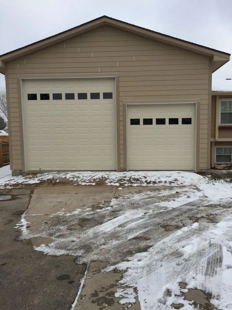 Two-car garage with beige doors and snow-covered driveway outside a house