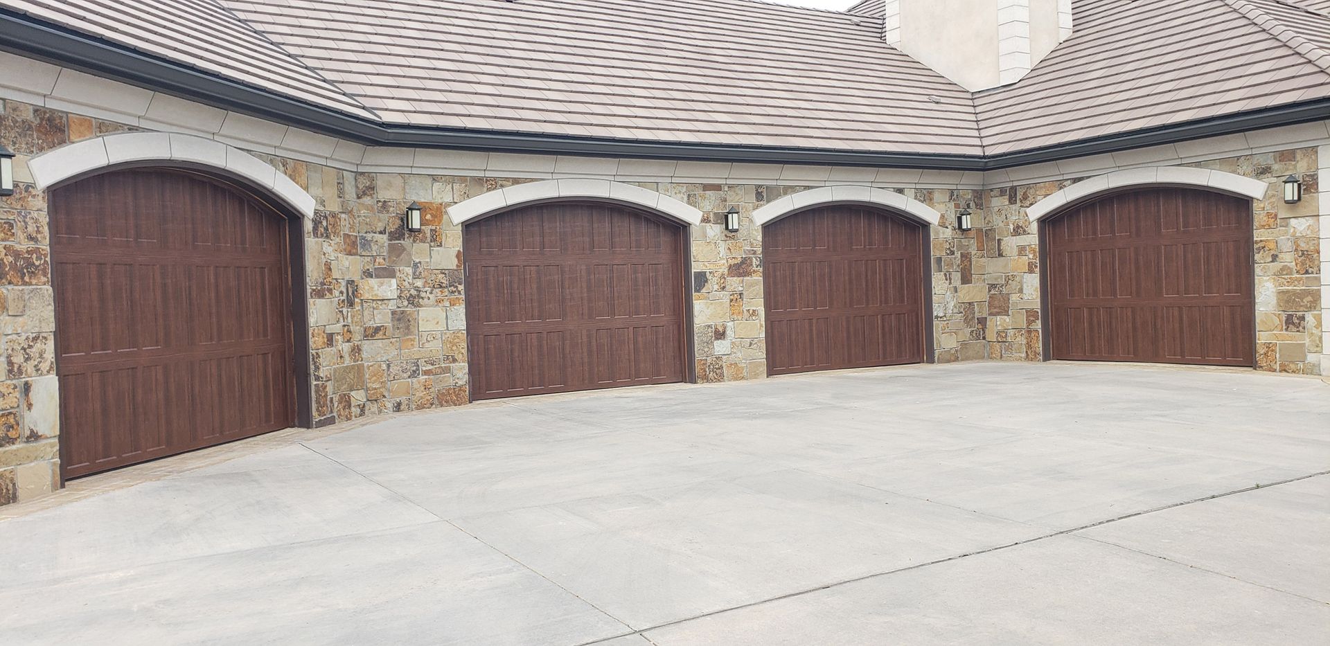 Four brown arched garage doors in a stone building. A concrete floor is in front.