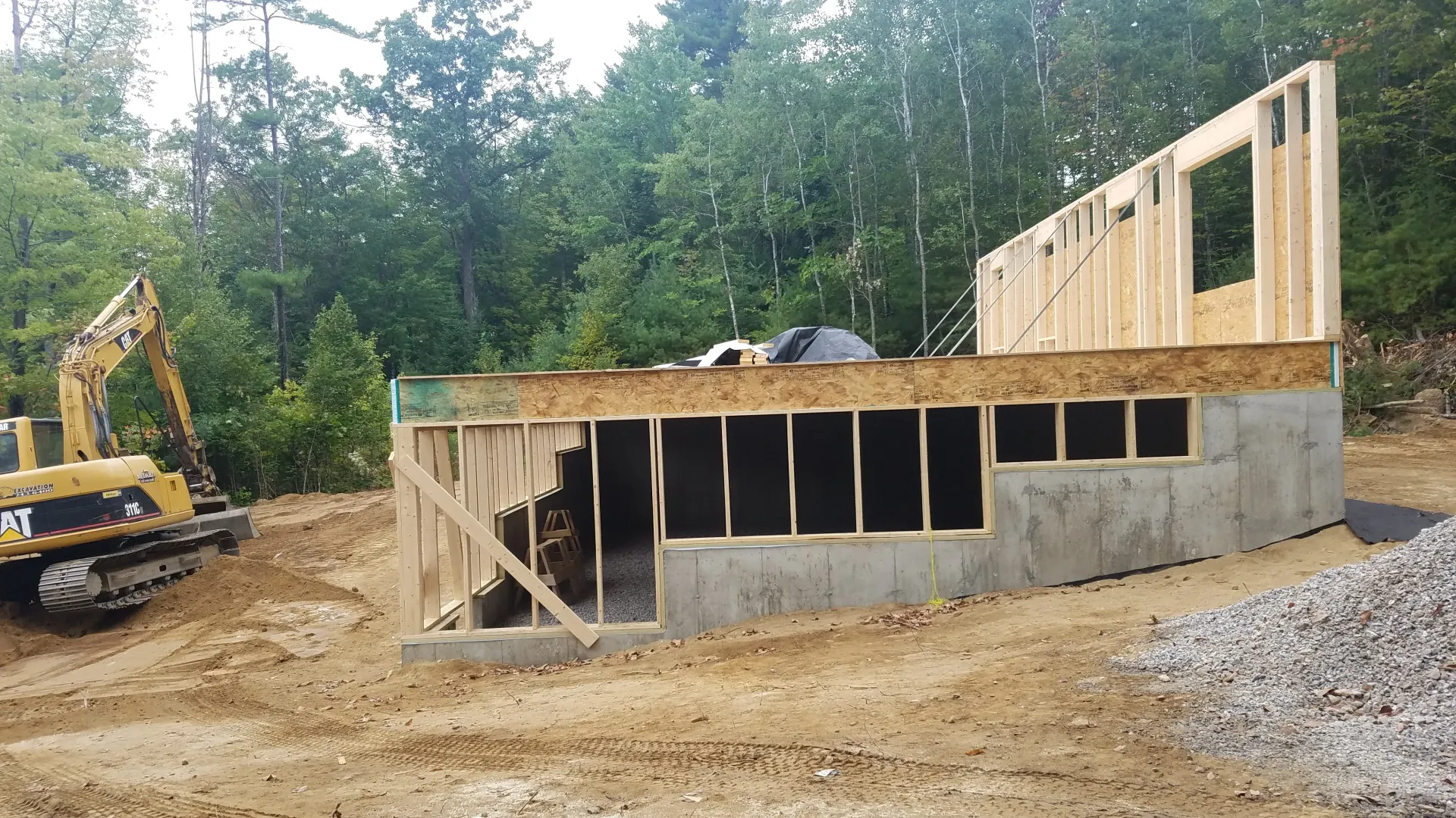 A house is being built in a dirt field with a bulldozer in the background.