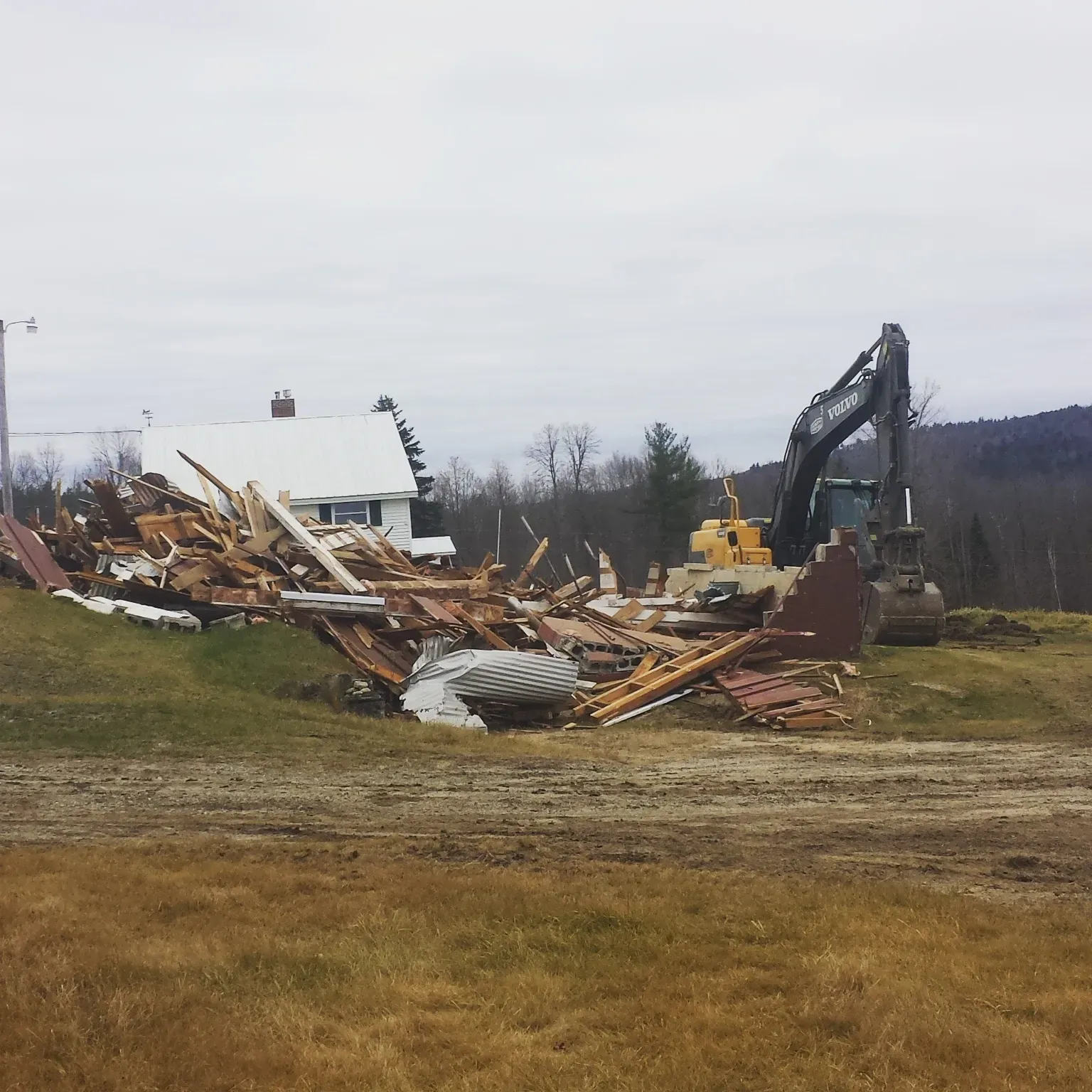 A house is being demolished by a bulldozer in a field