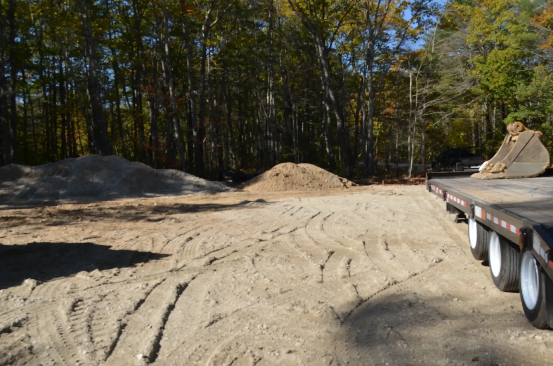 A semi truck is driving down a dirt road next to a pile of dirt.