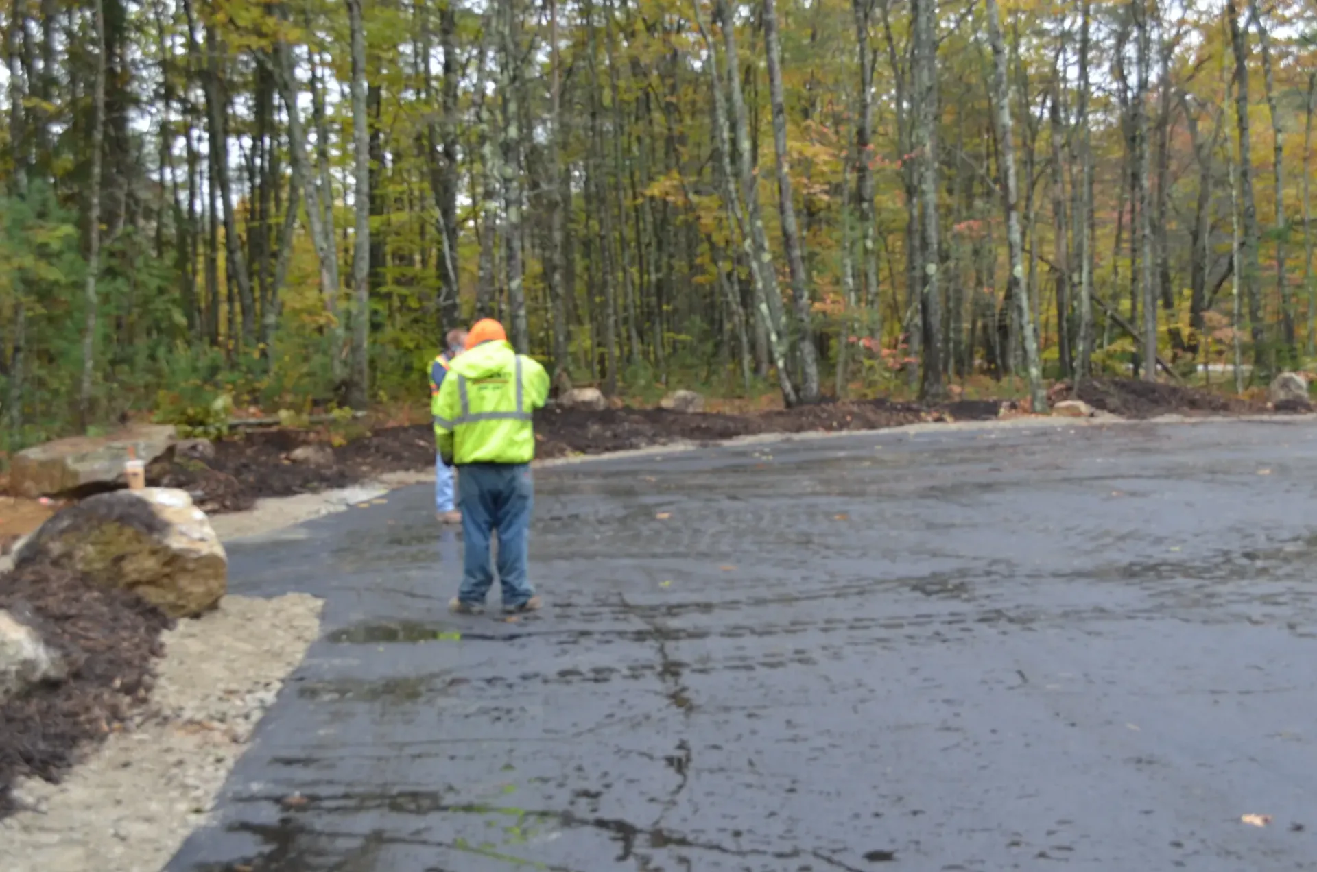 A man in a yellow vest is standing on a road in the woods.