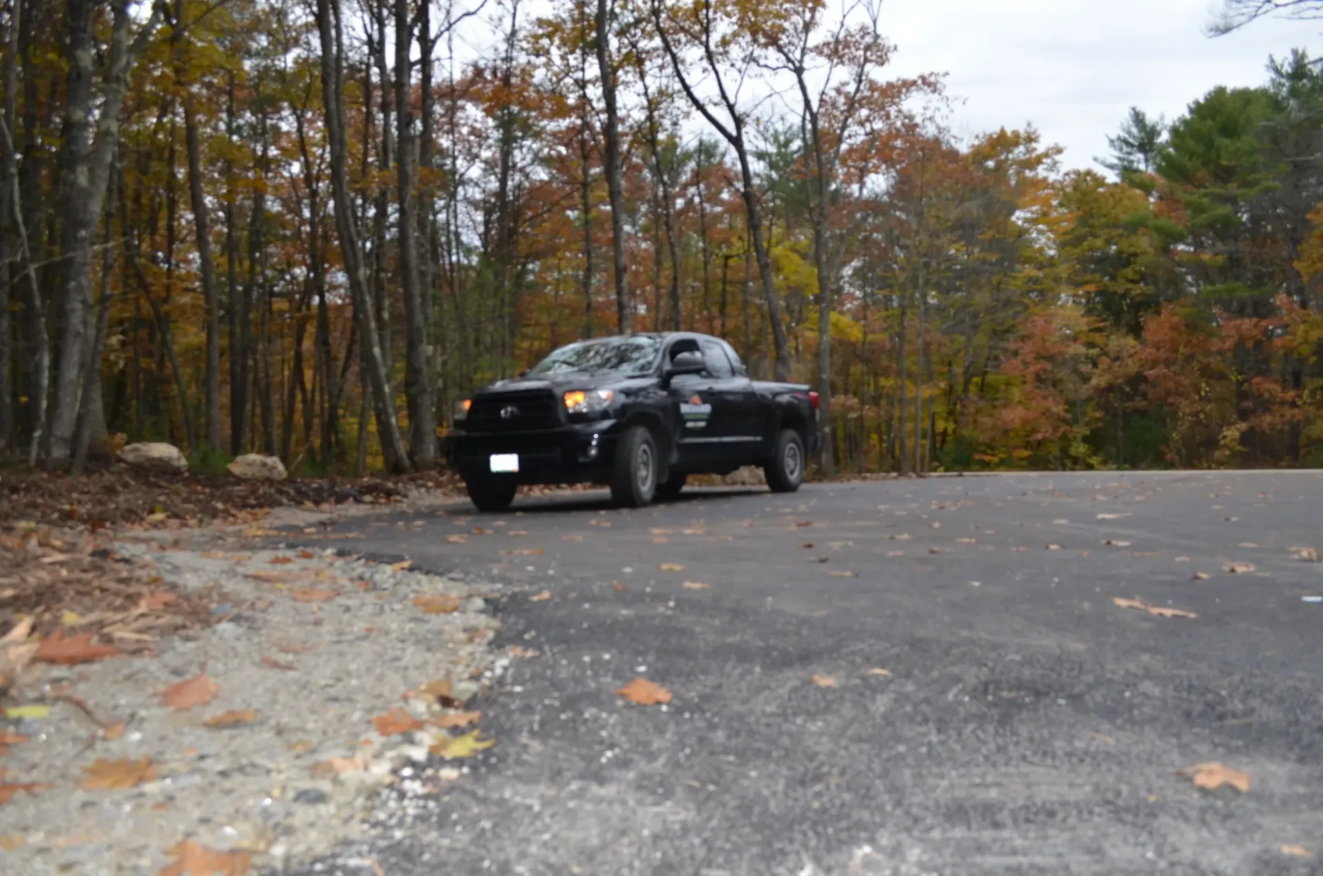 A black truck is parked on the side of a road in the woods