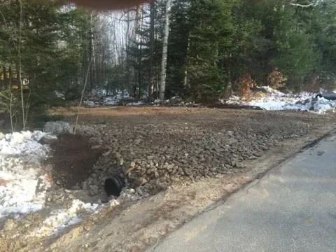 A hole in the ground next to a road with trees in the background