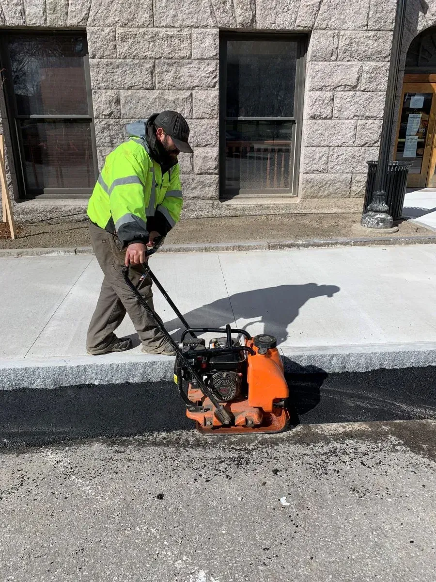 A man is using a machine to spread asphalt on a sidewalk.