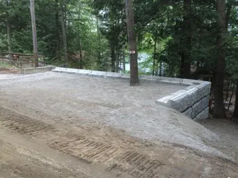 A large concrete wall is sitting on top of a dirt hill in the middle of a forest.