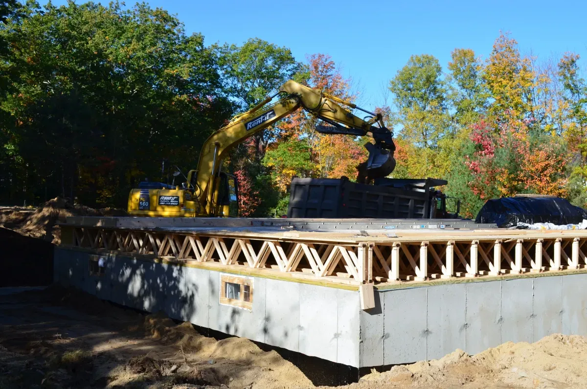 A yellow excavator is working on a concrete foundation.