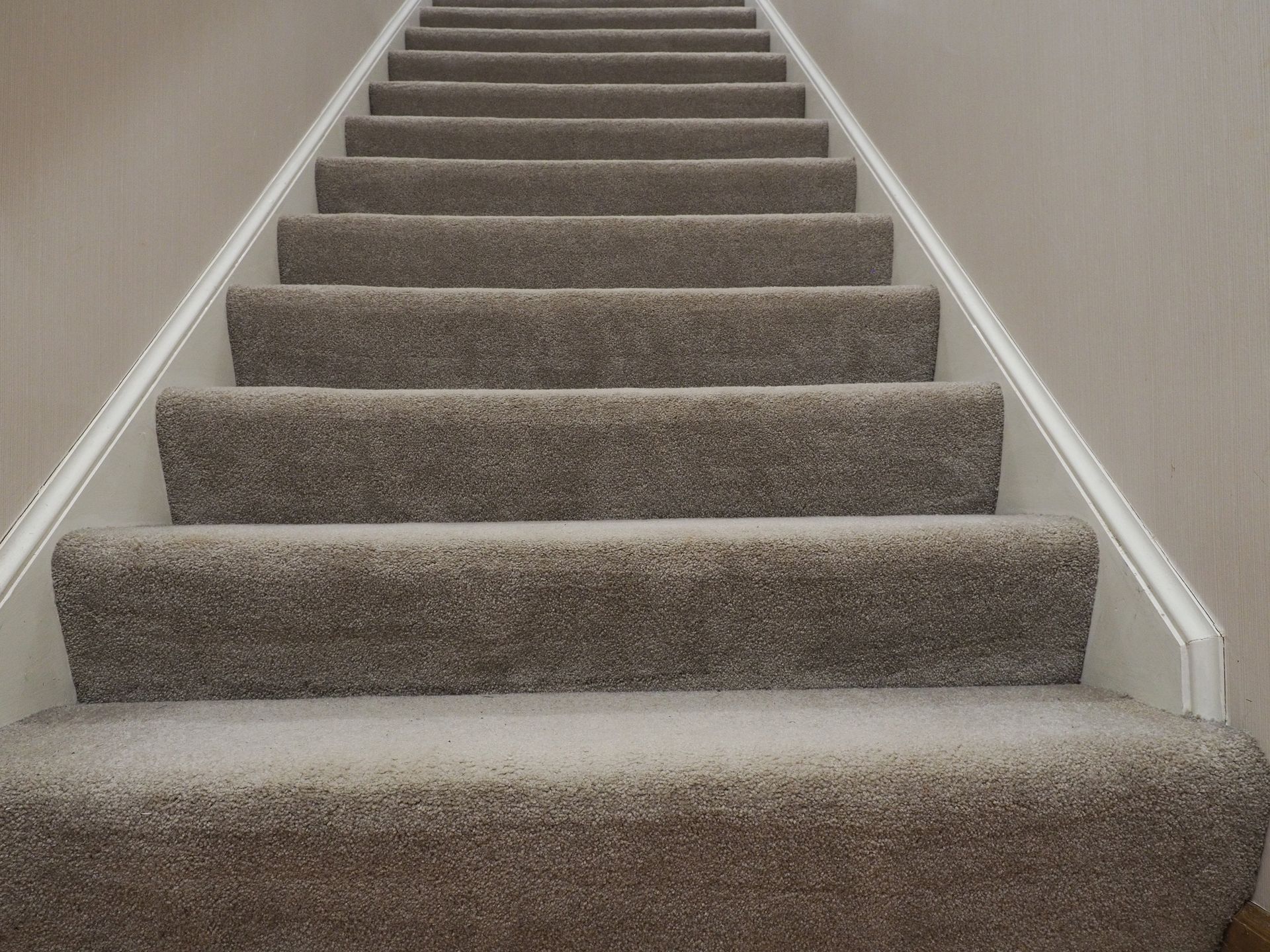 Carpeted staircase with beige walls and white trim, ascending upwards.