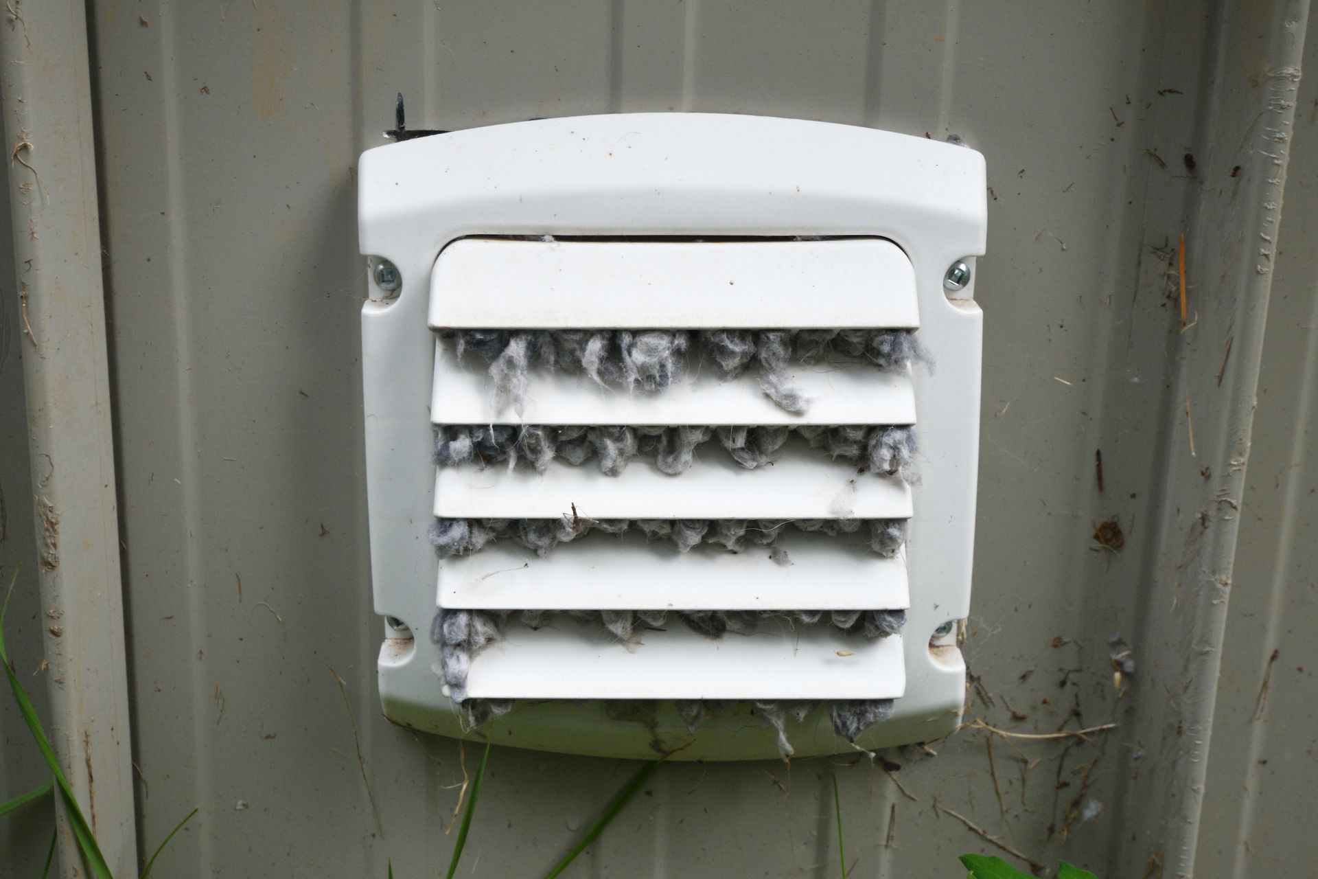 White dryer vent clogged with gray lint on a gray building.