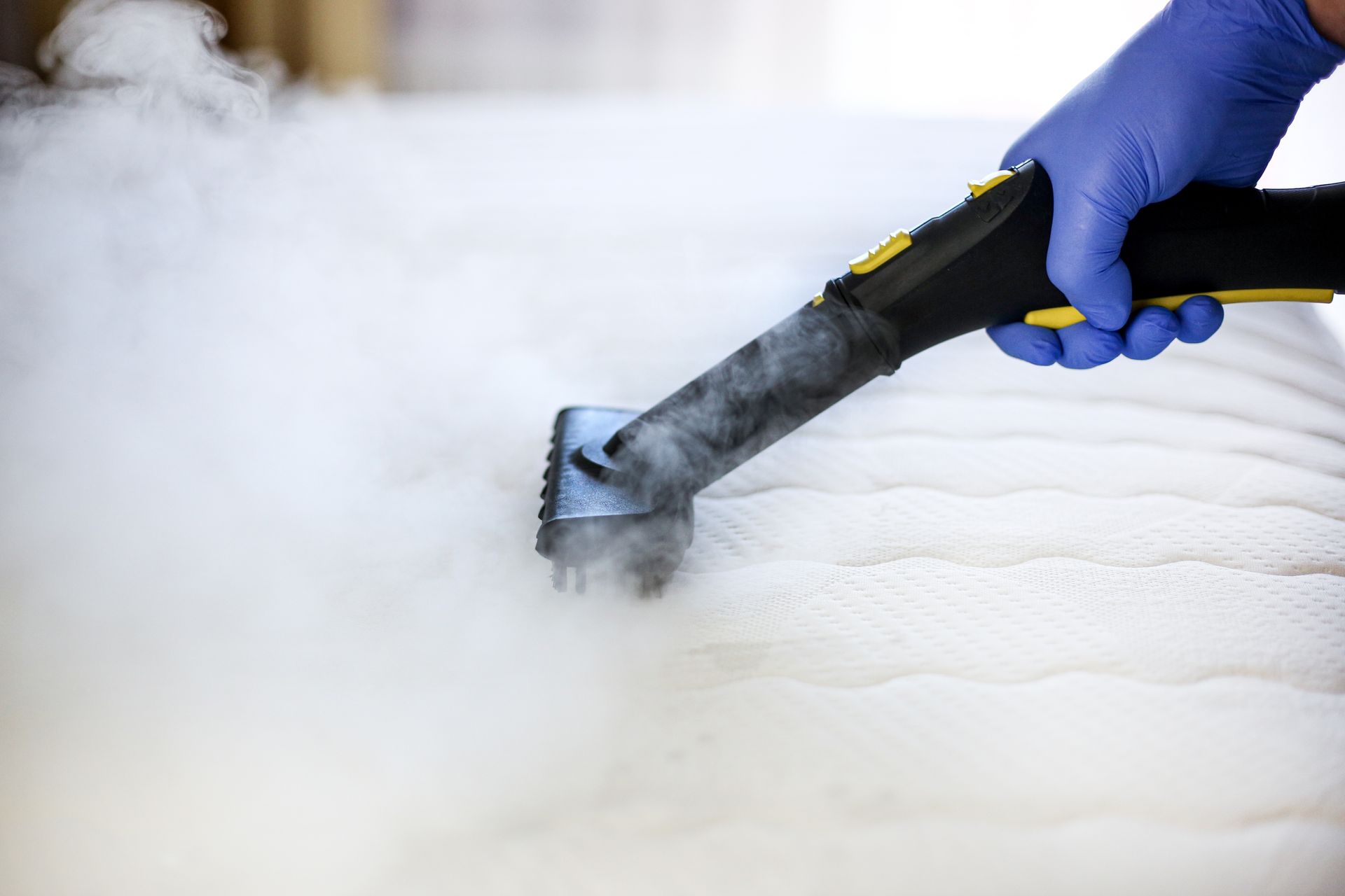 Person in blue gloves steam cleaning a white mattress.