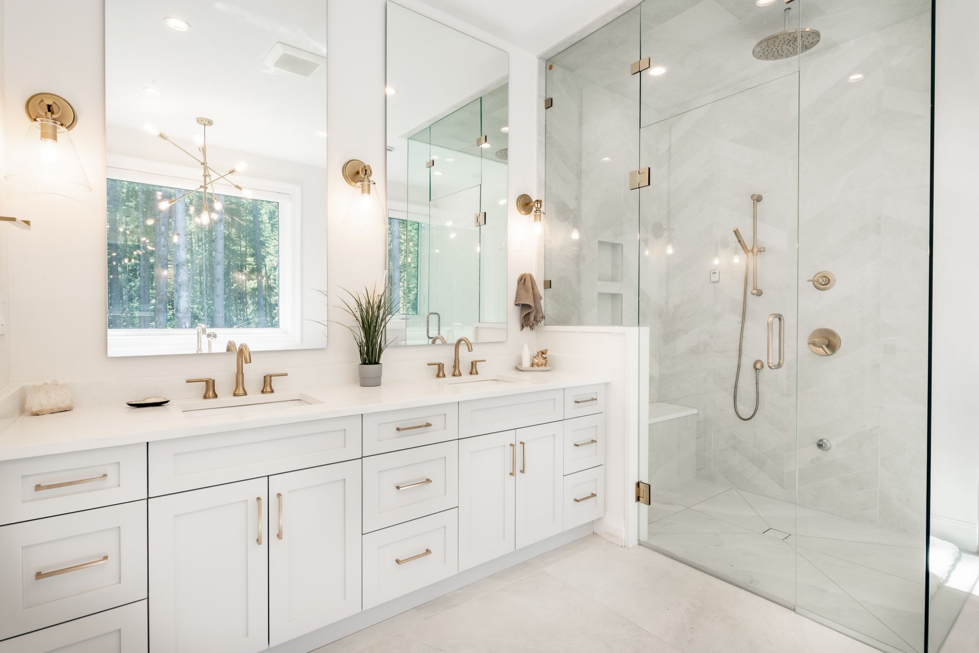 White bathroom with double vanity, glass shower, and gold fixtures.