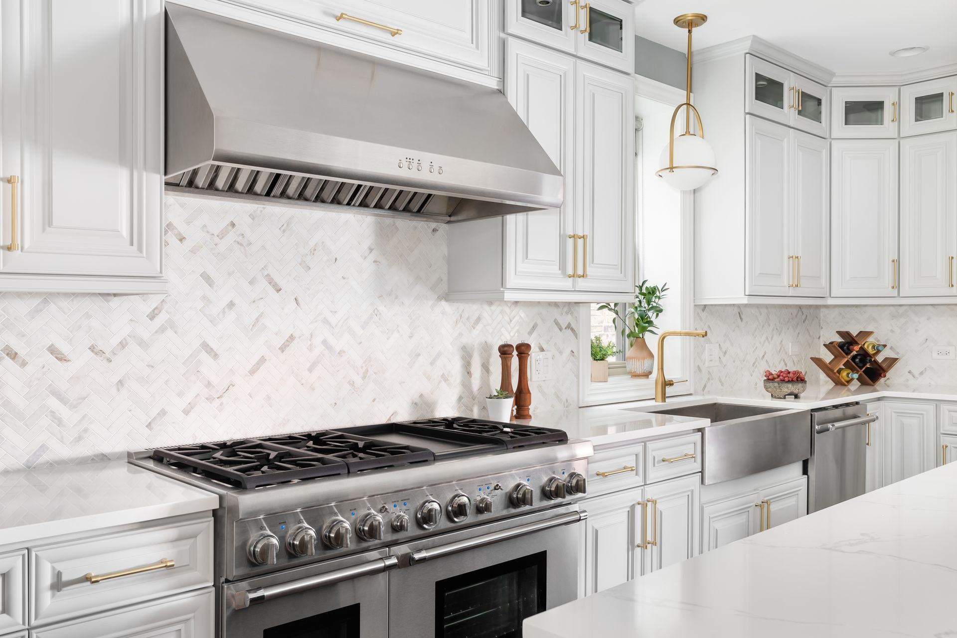 Stainless steel range hood over a stainless steel stovetop in a white kitchen.