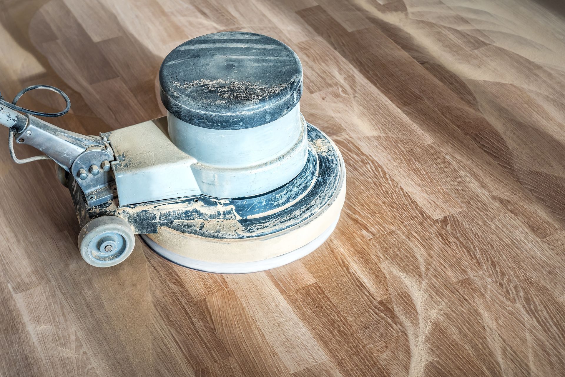 Floor buffer machine on a wood floor, with a dusty white base and metal handle.