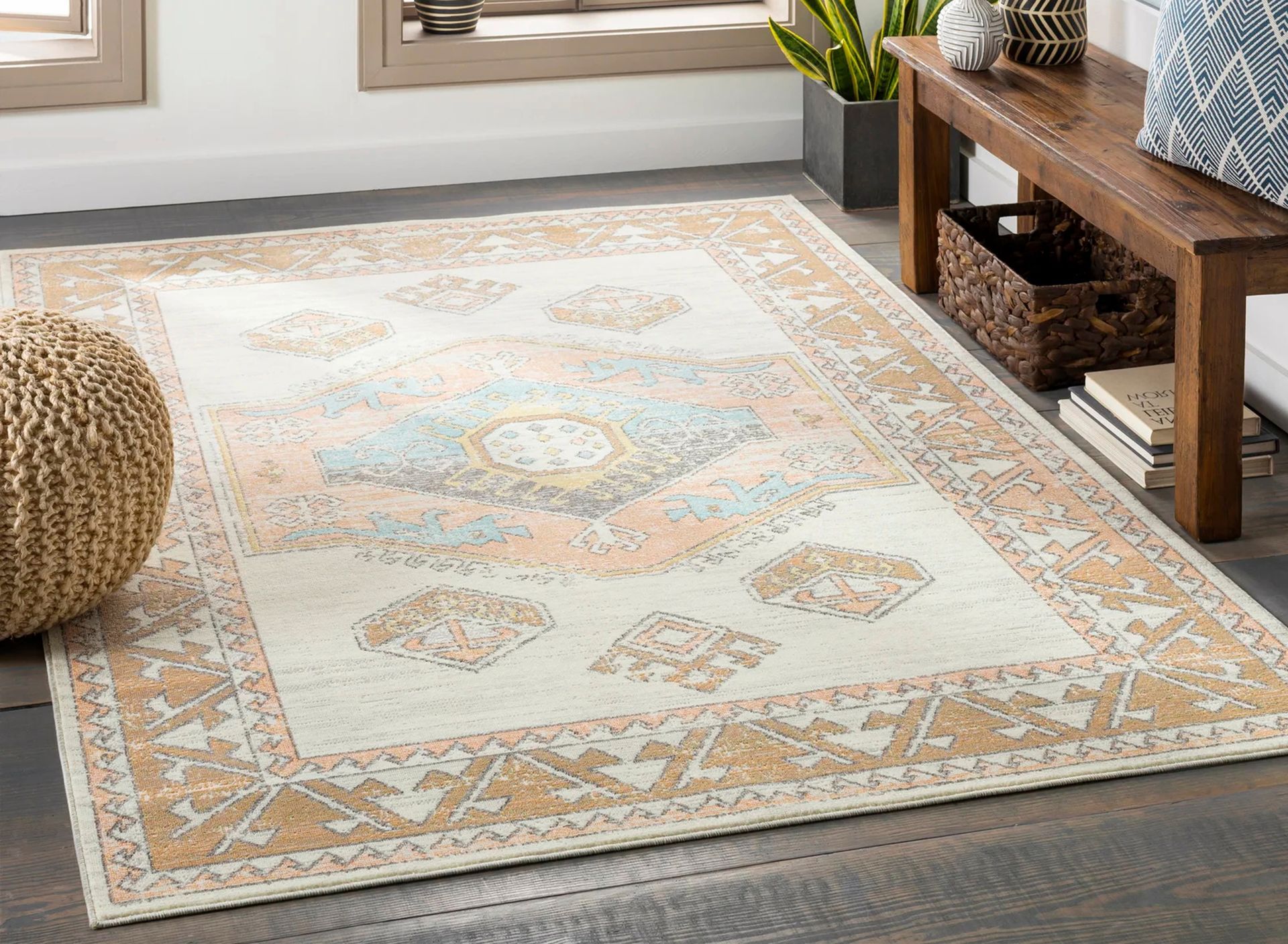 Beige and peach patterned rug on a wooden floor, with a bench and ottoman in the background.