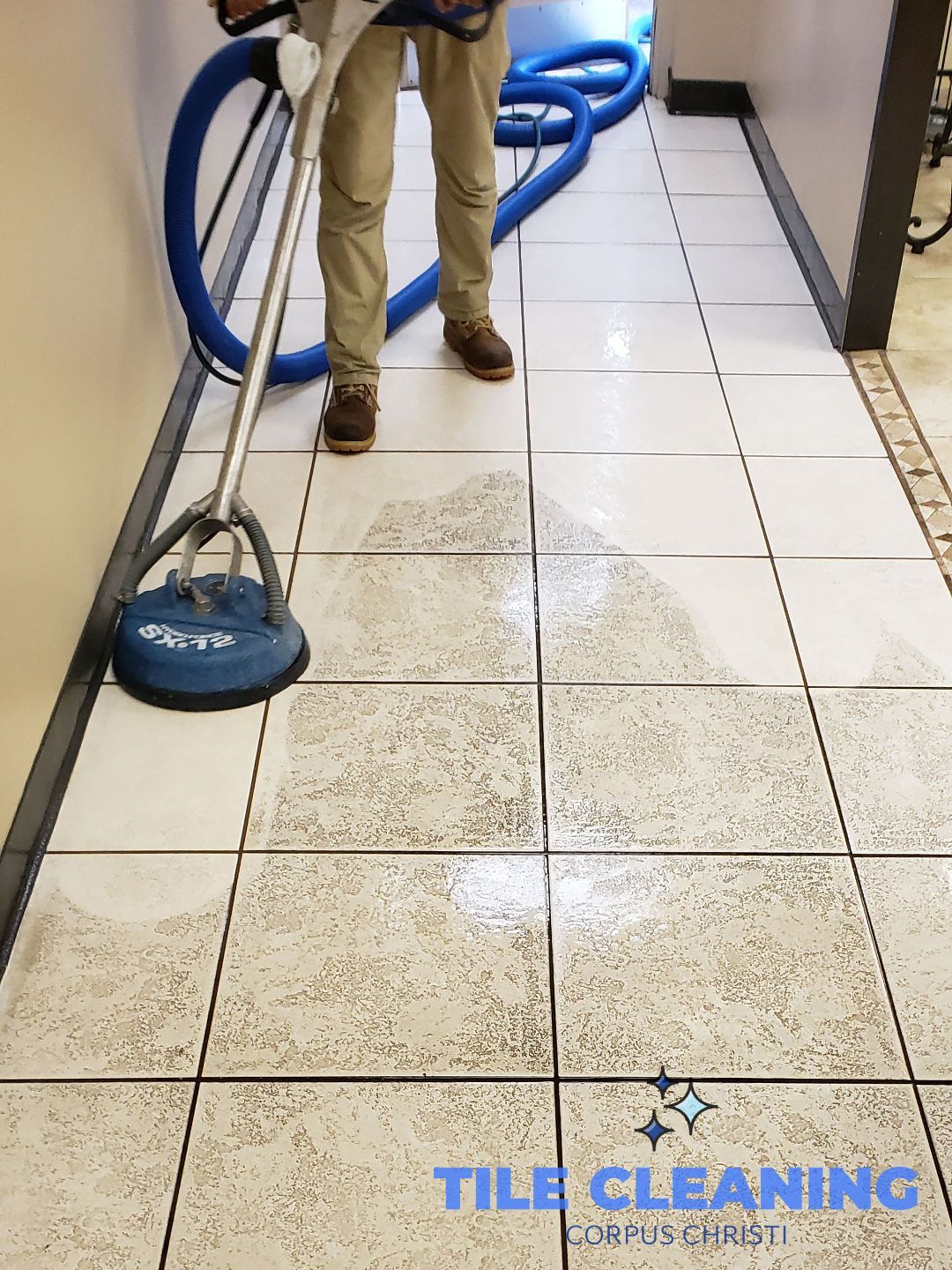 Worker cleaning dirty tile floor with a blue floor scrubber in a hallway