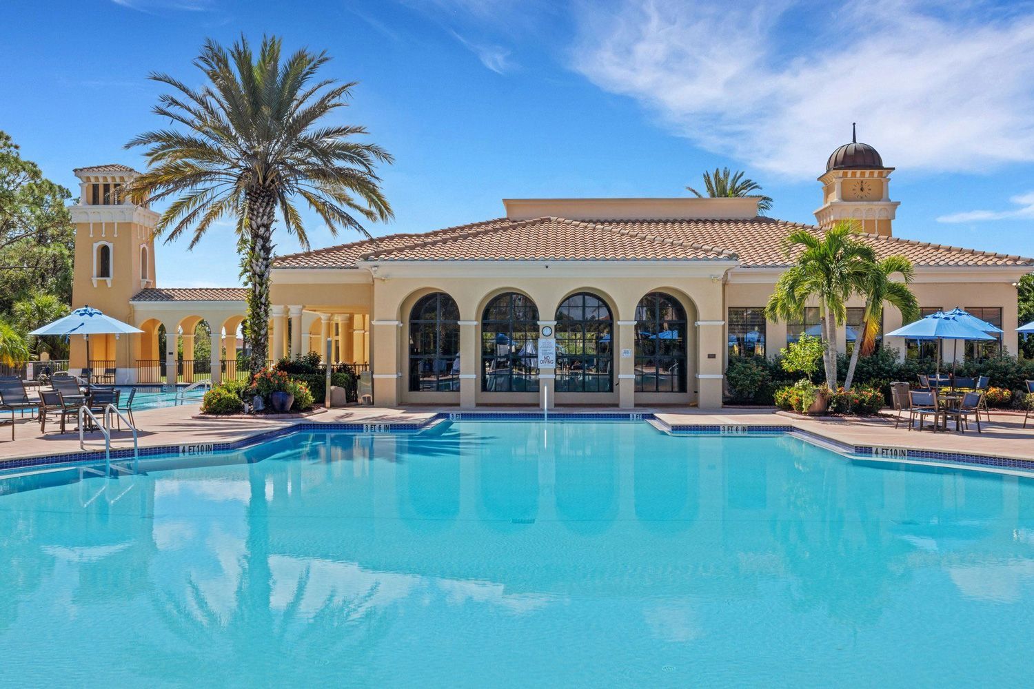 Swimming pool in front of a tan building with arched windows and a dome, under a blue sky.