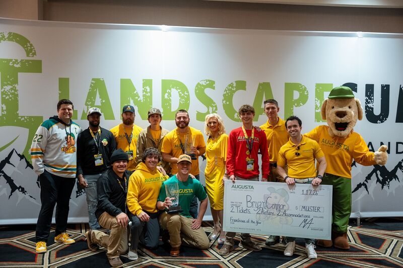 Group pose at Landscape Summit with a mascot, holding a large check with logo background.