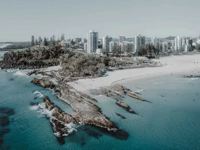 Aerial view of a sandy beach with rocky shoreline and turquoise water beside coastal high-rise buildings