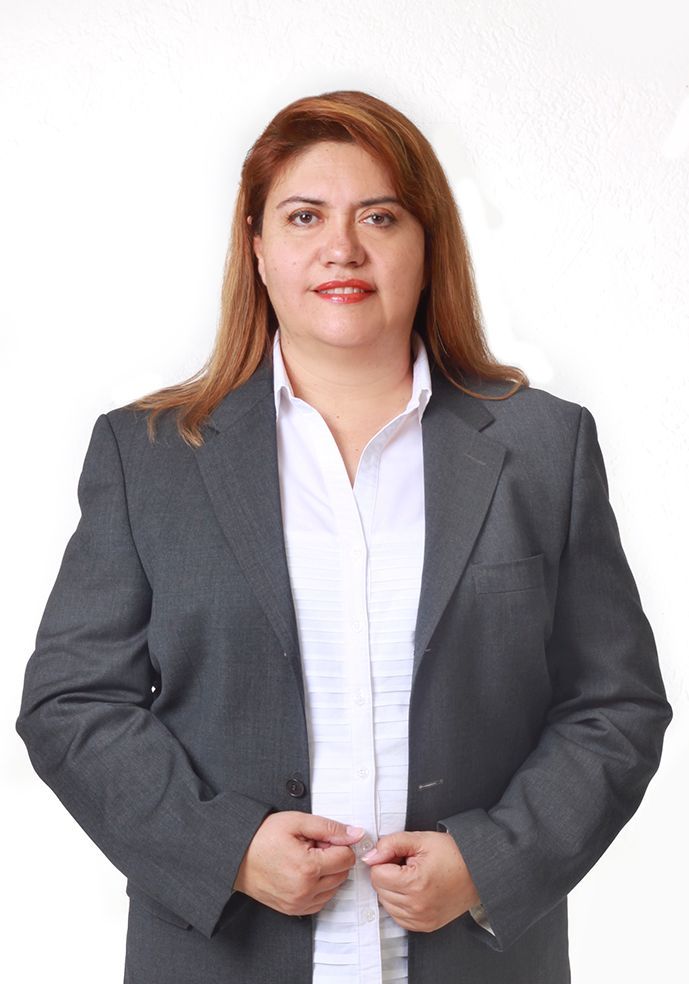 Mujer con blazer gris y camisa blanca, parada frente a la cámara.