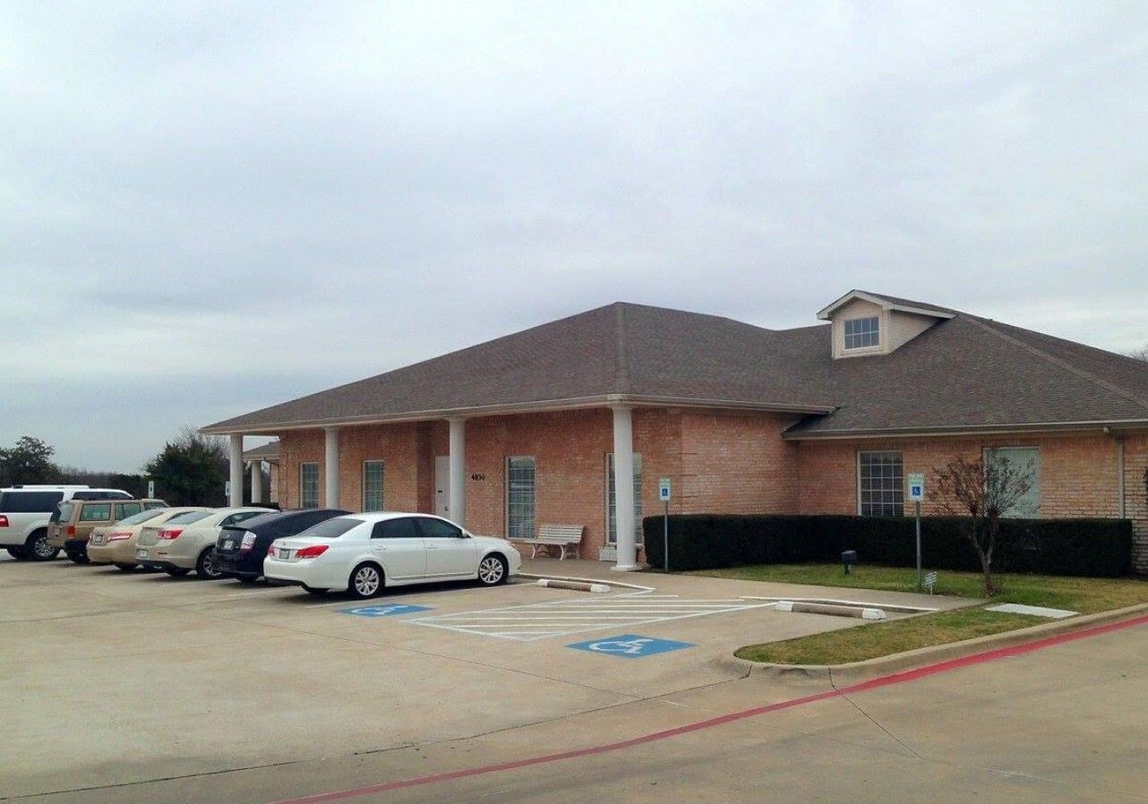 Brick office building with parked cars and cloudy sky, viewed from the parking lot