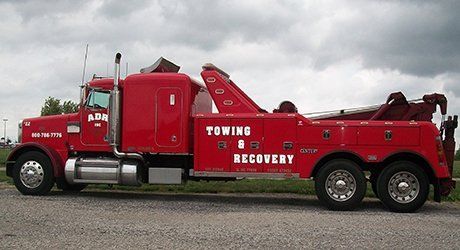 Red towing and recovery tow truck parked on a road under cloudy sky