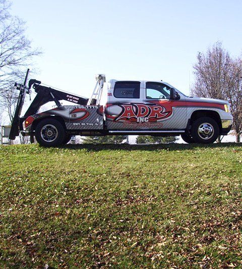Tow truck parked on grass, side view, with red and gray ADR graphics on the cab and bed.