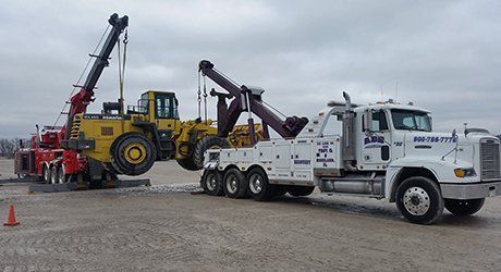 Tow trucks and heavy equipment lined up on a snowy gravel lot under a gray sky