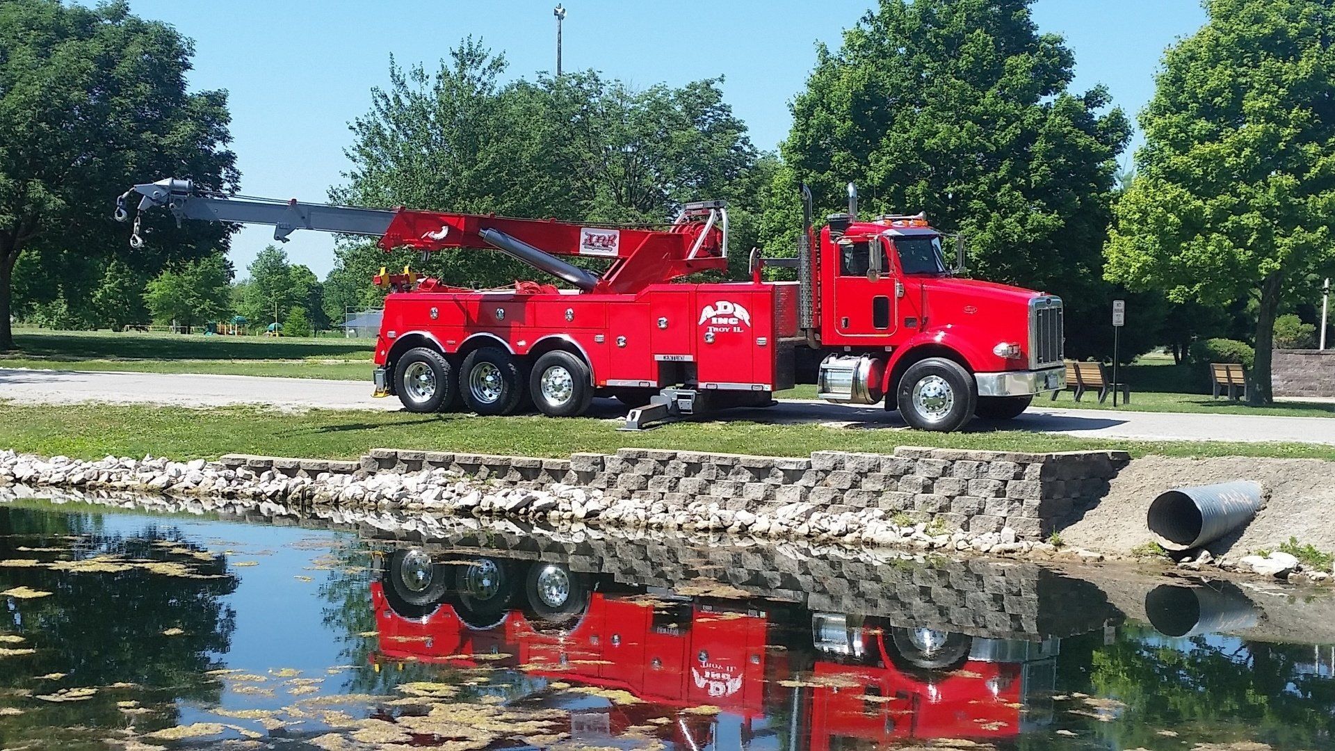 Red utility truck parked by a pond, with its reflection visible in the water.