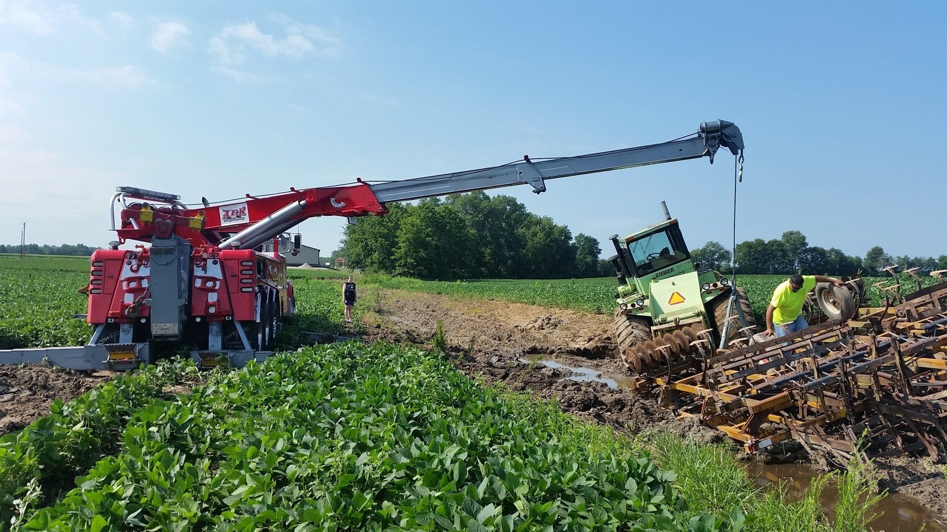 Harvesting machine loading root crops in a field, with workers nearby under a blue sky