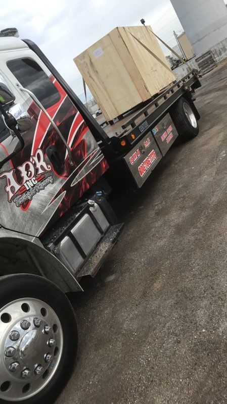 Flatbed truck carrying a large wooden crate in an industrial yard.