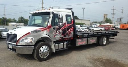 White flatbed tow truck parked on gravel lot under overcast sky