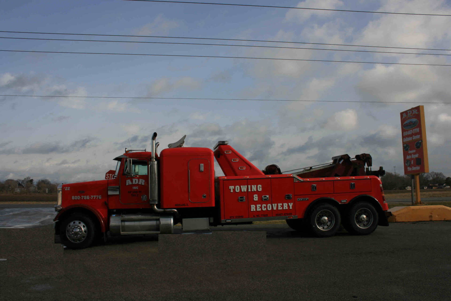 Red semi-truck with rescue markings parked roadside under a cloudy sky