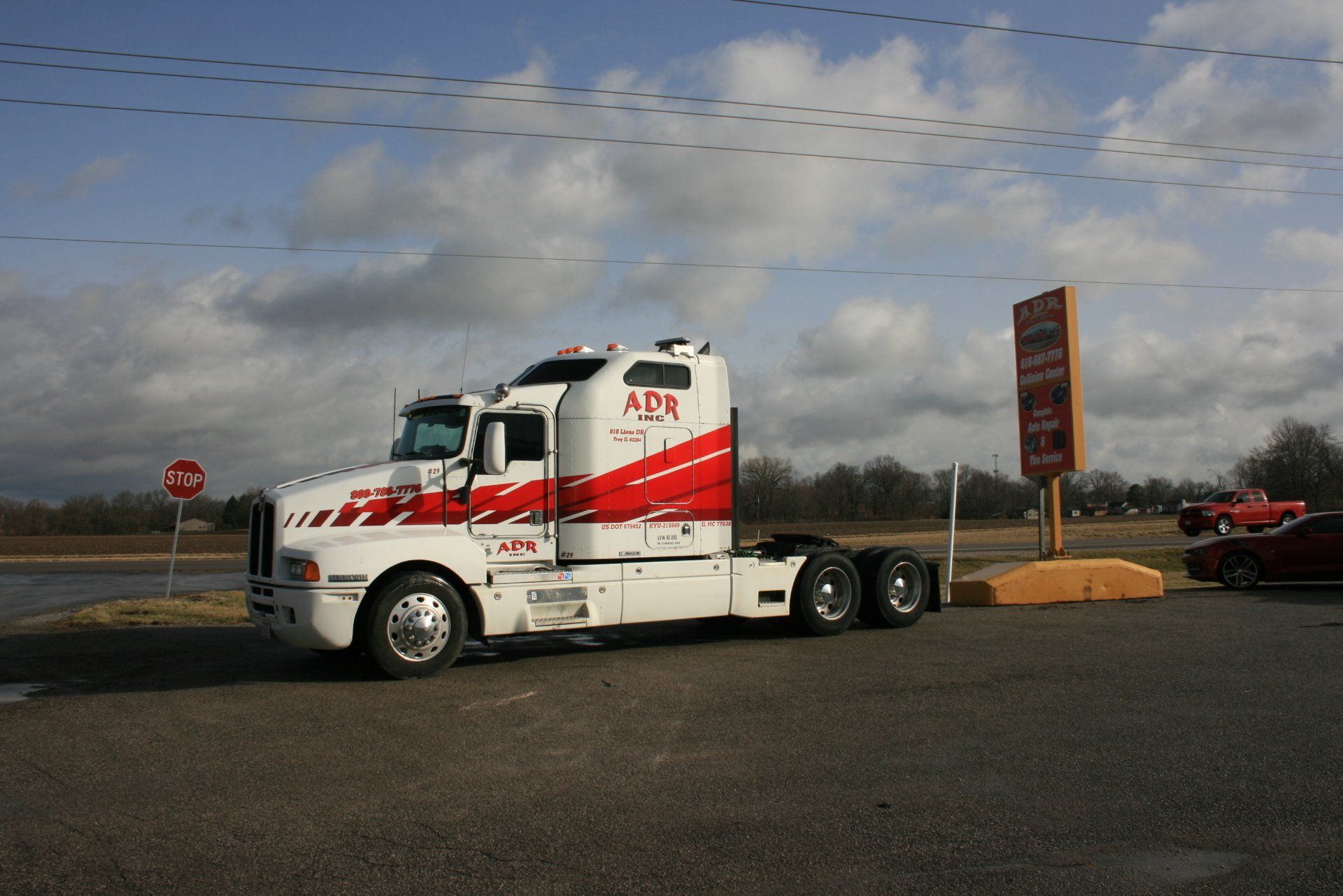 White ADO semi-truck parked by a roadside sign under a cloudy sky