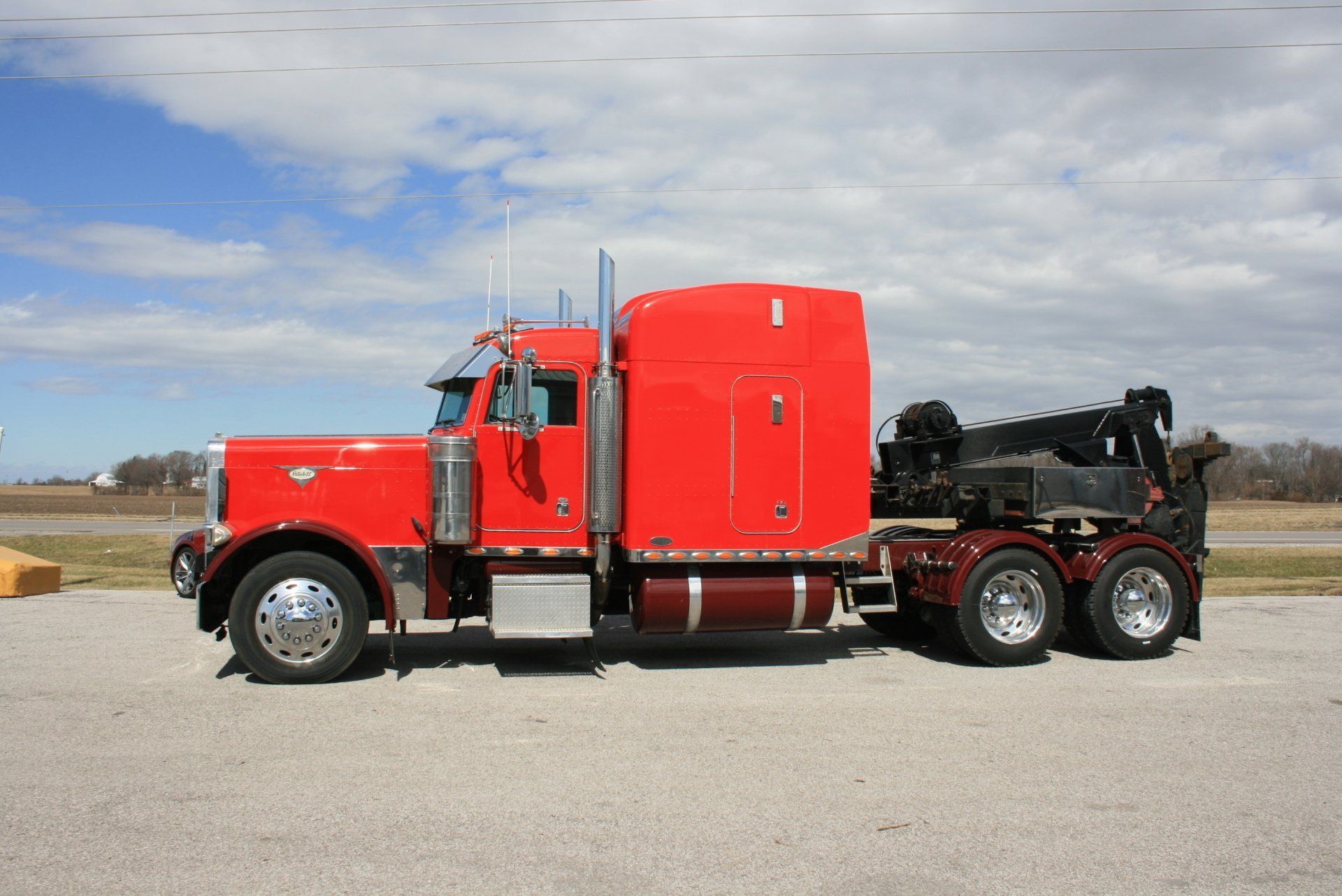 Red semi truck with sleeper cab and black chassis parked on a road under a cloudy sky