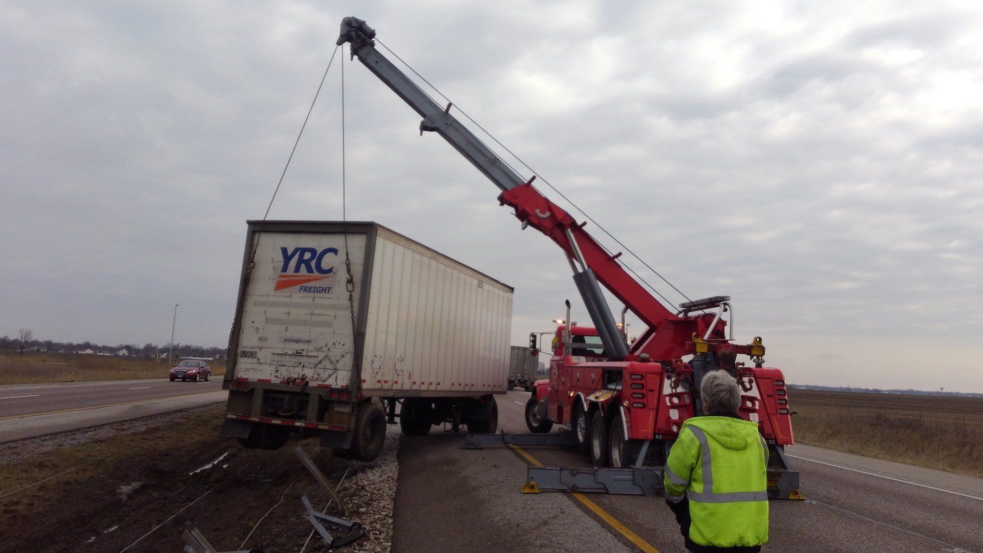 Tow truck lifting a YRC semi-trailer on a wet highway, with workers nearby under cloudy skies