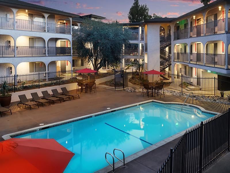 A large swimming pool surrounded by chairs and umbrellas in front of a hotel.