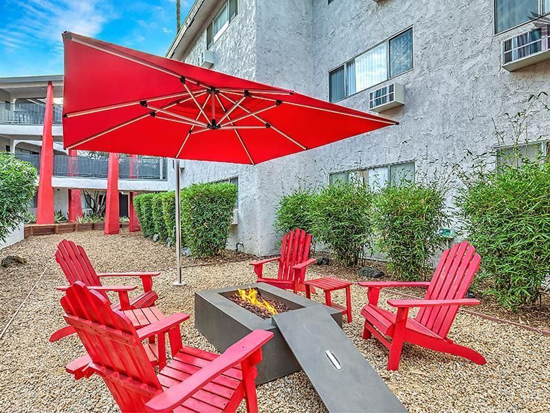 A fire pit with red chairs and an umbrella in front of a building.