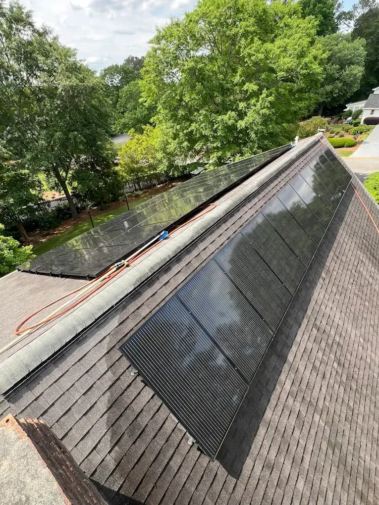 Solar panels installed on a residential rooftop. Brown shingles, trees in the background, blue sky.