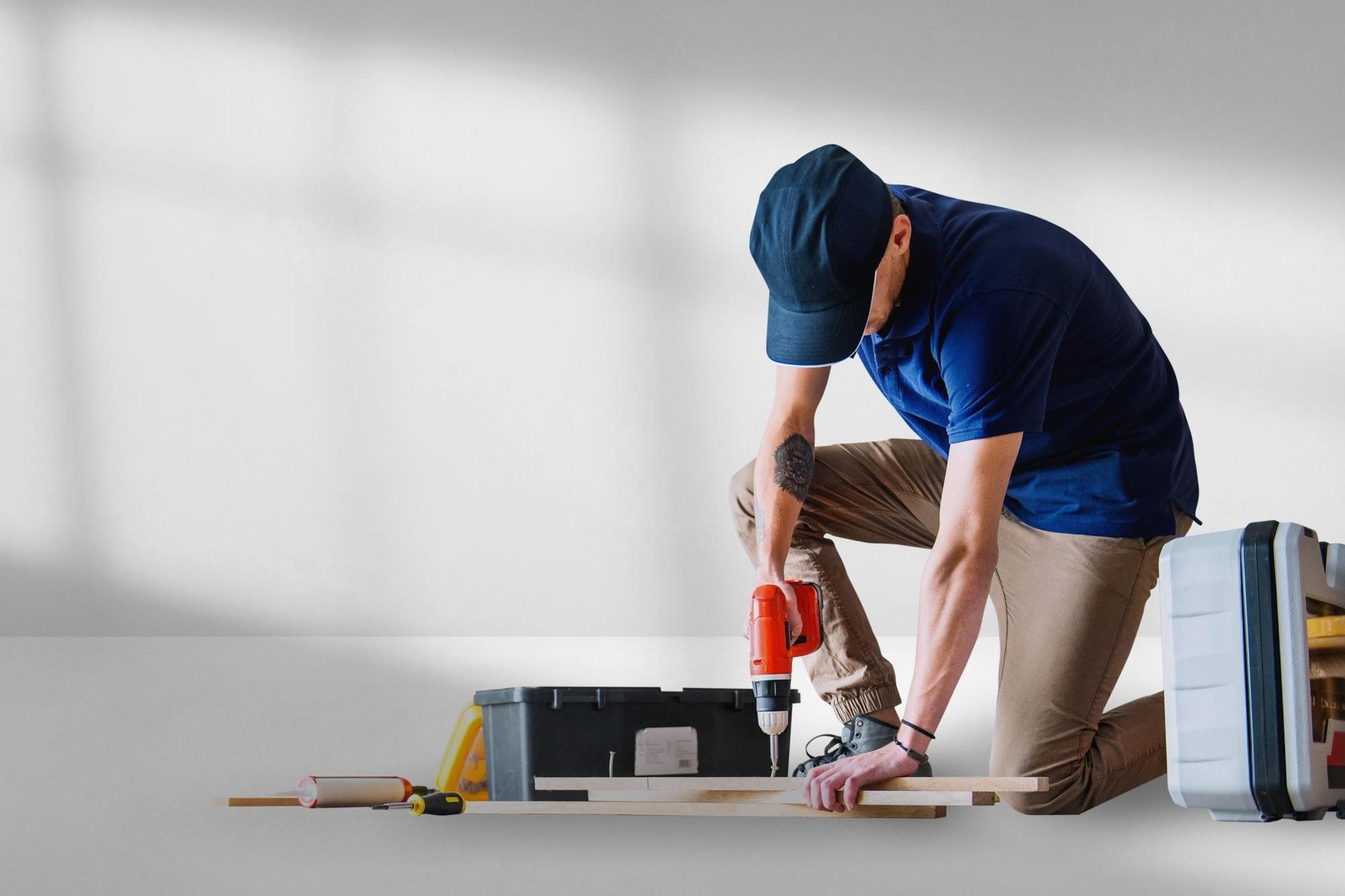 Worker kneeling on floor using a red drill near tools and a box in a bright room