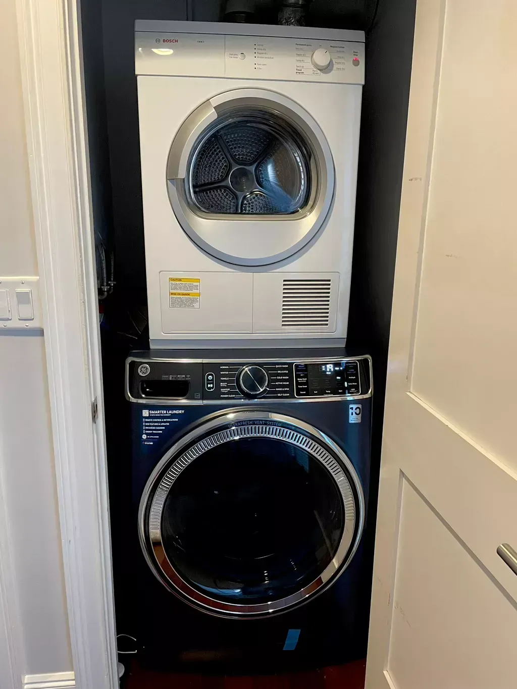 Stacked washer and dryer in a narrow laundry closet, white dryer on top and black washer below