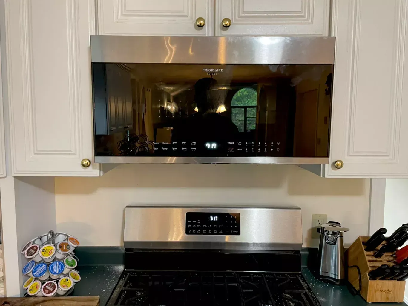 Kitchen stove and microwave under white cabinets with dark countertops and utensils on both sides