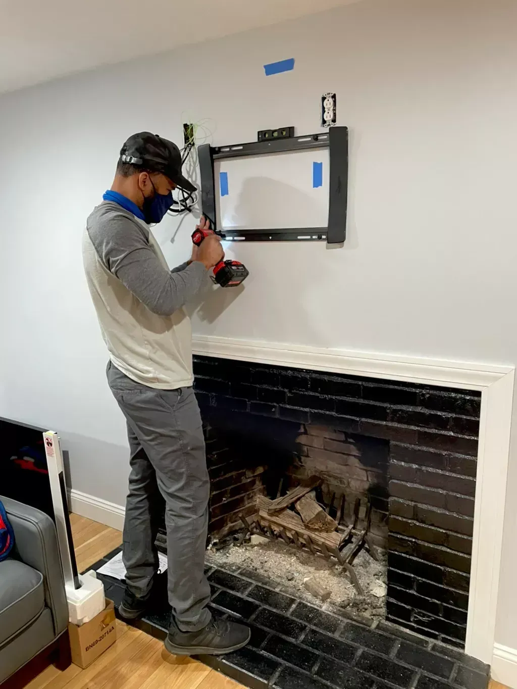 Person installing a wall-mounted TV bracket above a fireplace in a living room