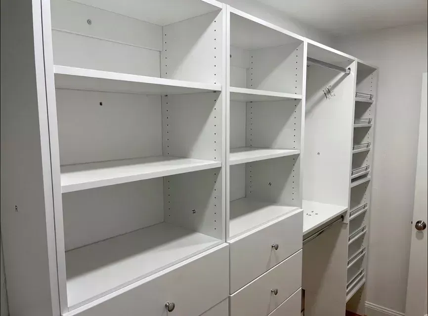 White built-in closet with open shelves, drawers, and hanging space in a bright hallway or bedroom.