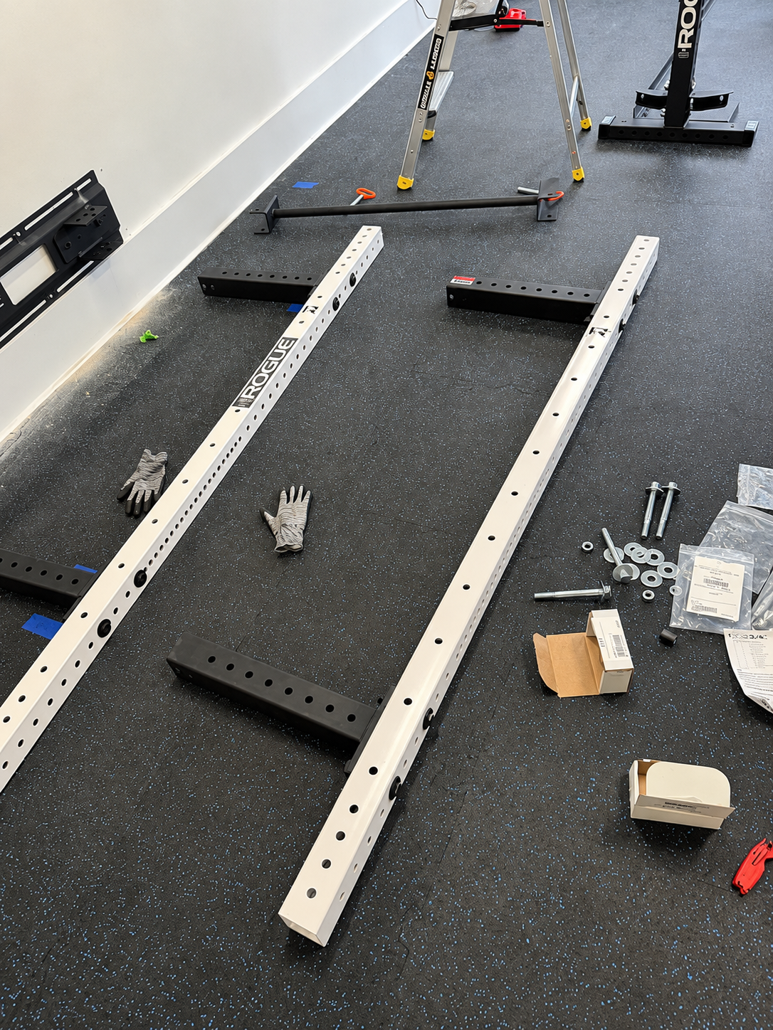 Disassembled metal bed frame parts scattered on a black floor in a room under construction