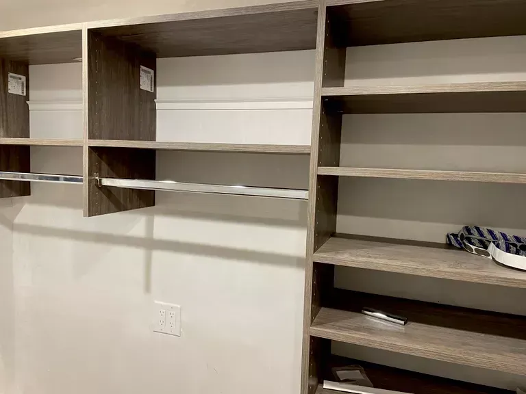 Built-in closet shelves with open compartments and a hanging rod in a beige room