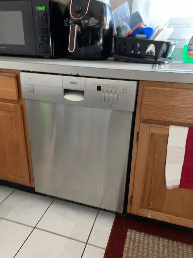 Stainless steel dishwasher under a kitchen counter beside wooden cabinets and small appliances.
